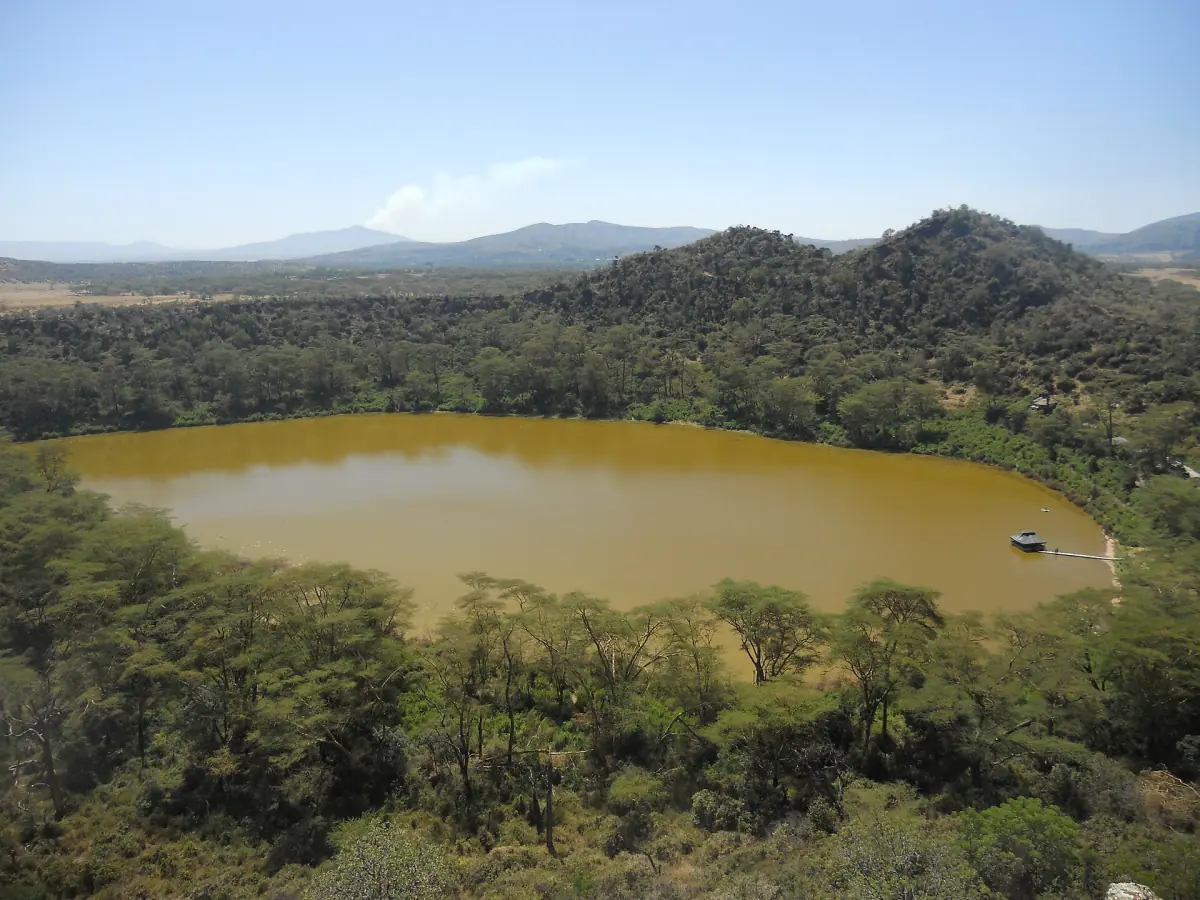 Small crater lake with green water inside a forested volcanic rim